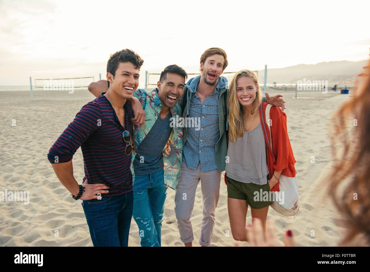 Gruppo di amici in piedi insieme sulla spiaggia, ridendo Foto Stock