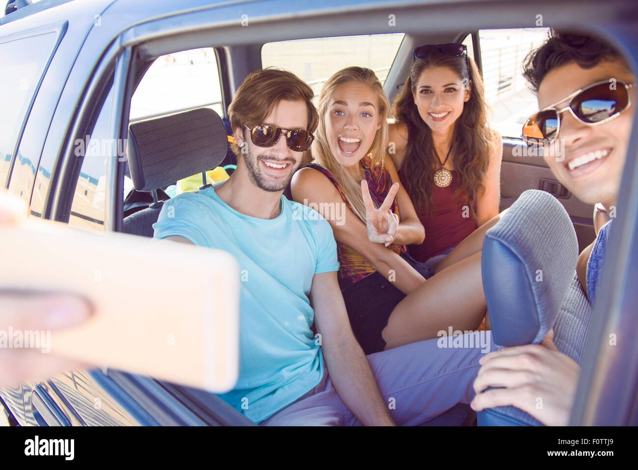 Gruppo di amici seduti in auto prendendo autoritratto con lo smartphone, ridendo Foto Stock