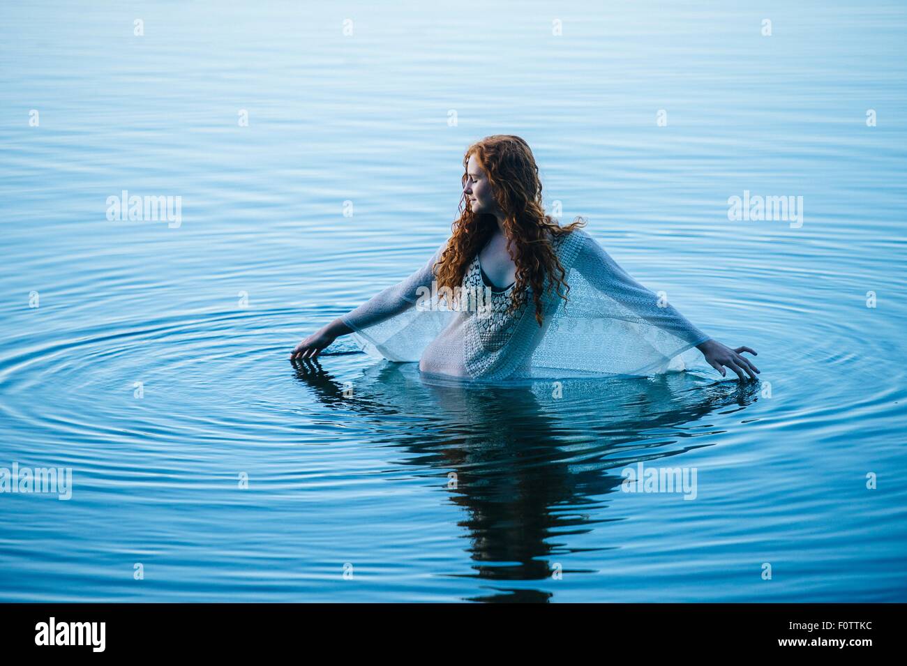 Giovane donna in piedi nel lago blu increspa la superficie con le dita Foto Stock