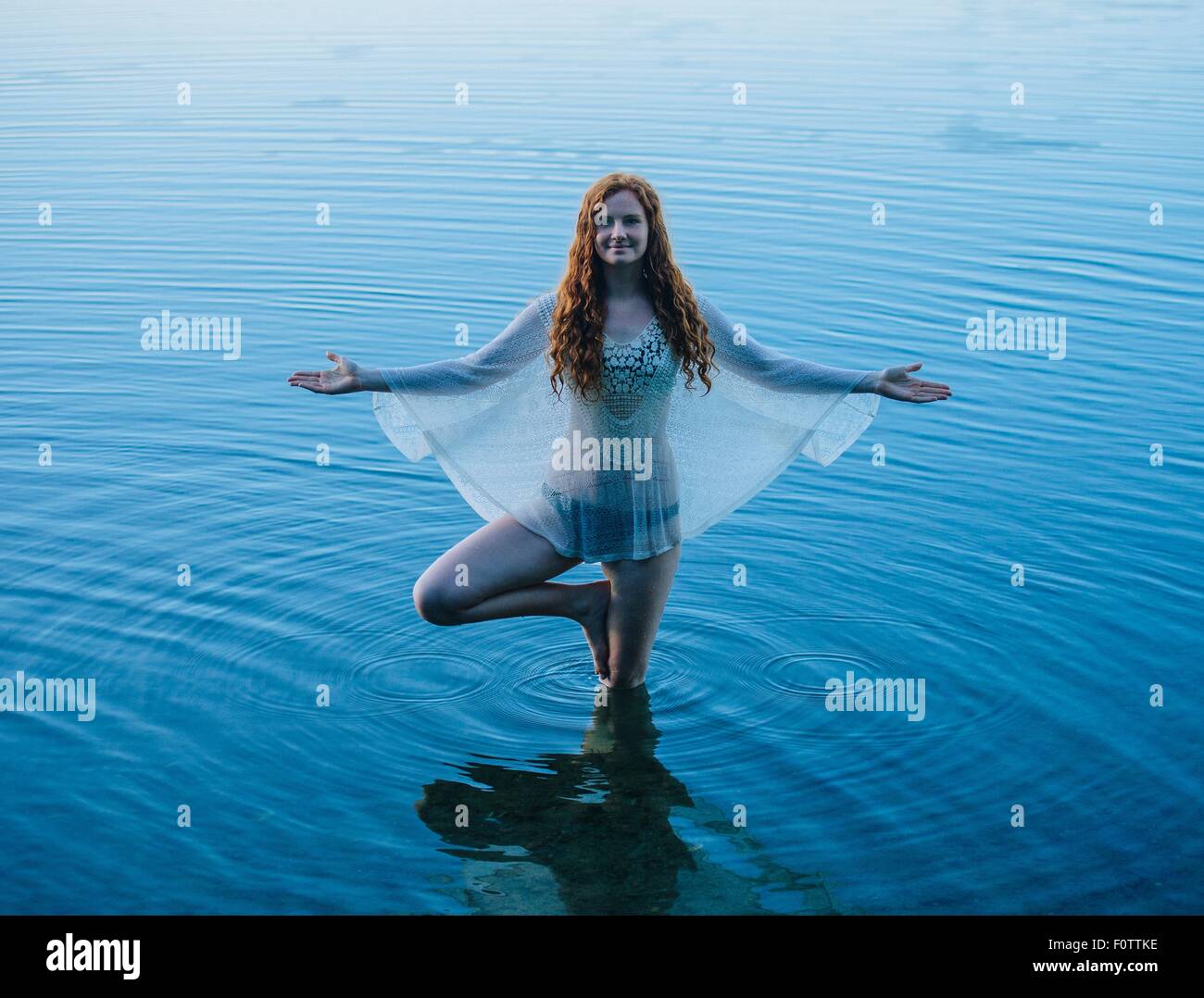 Giovane donna in piedi nel lago blu a praticare yoga Foto Stock