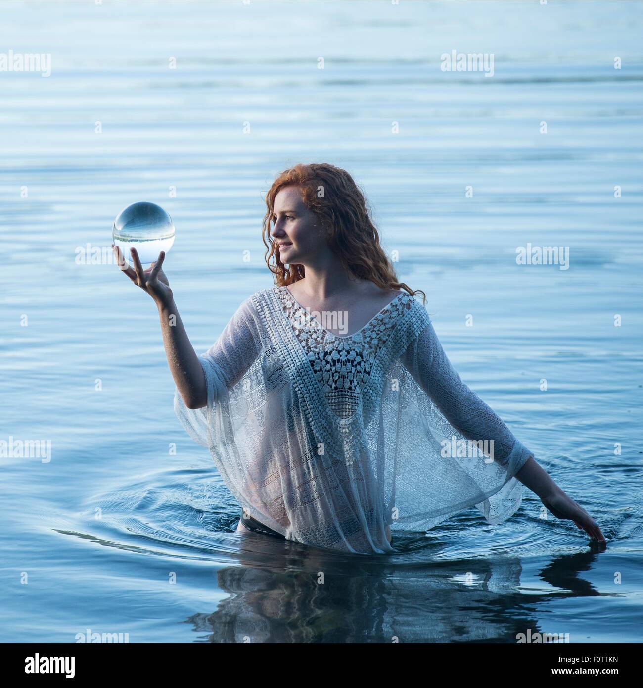 Giovane donna in piedi nel lago di sguardo sulla sfera di cristallo Foto Stock