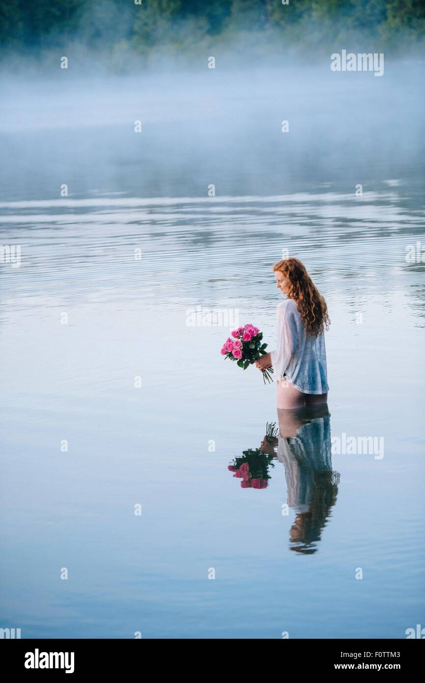 Giovane donna in piedi nel lago misty holding mazzo di rose rosa Foto Stock