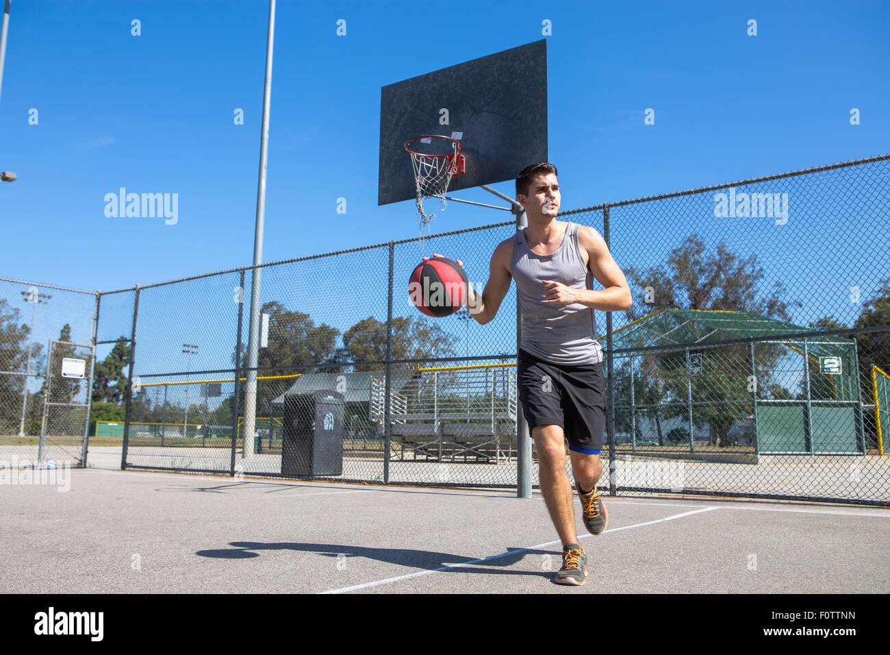 Maschio giovane giocatore di basket in esecuzione con la palla sul campo di pallacanestro Foto Stock