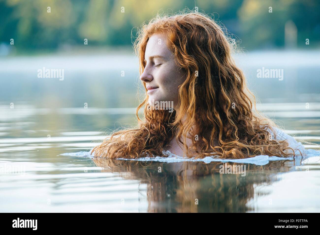 La testa e le spalle del giovane e bella donna con gli occhi chiusi nel lago Foto Stock