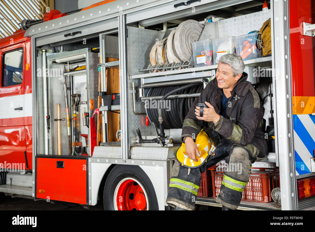 Felice fireman seduta nel carrello alla stazione dei vigili del fuoco Foto Stock