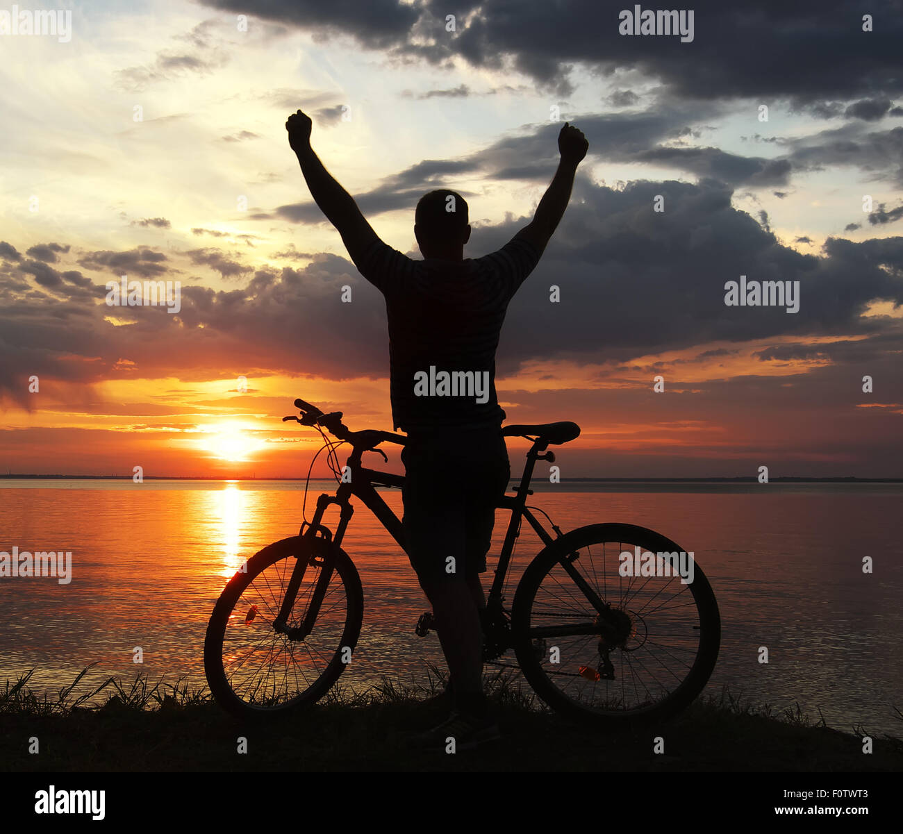 Silhouette di un uomo con una mountain bike sulla riva del fiume al tramonto Foto Stock