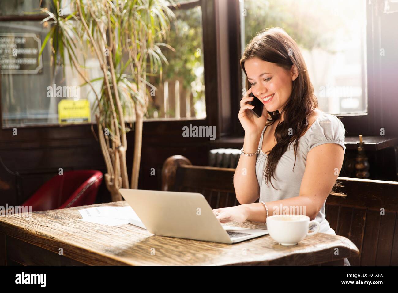 Metà donna adulta seduta utilizzando laptop e sorridente dello smartphone Foto Stock