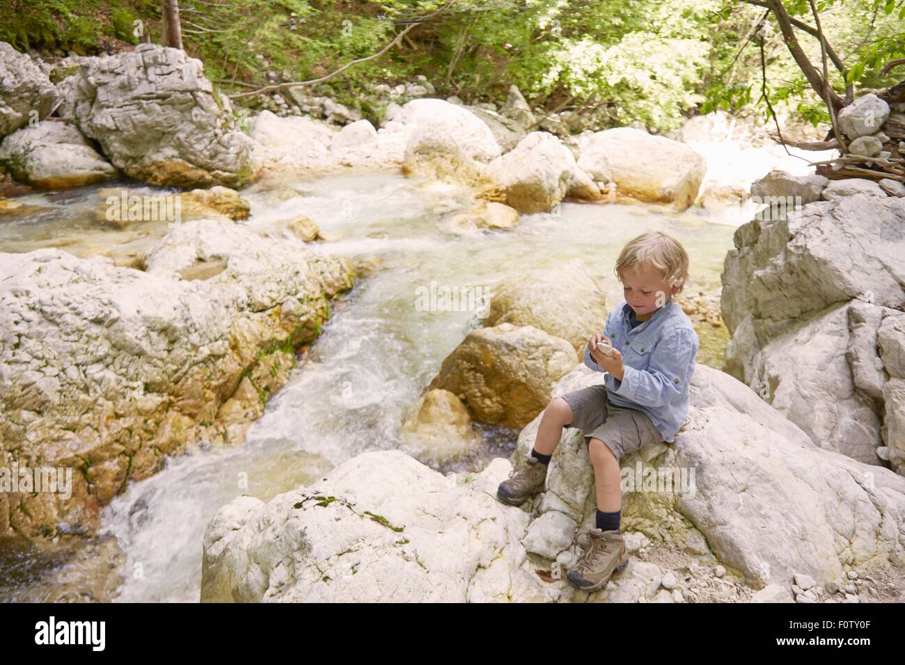 Ragazzo seduto sulle rocce dal fiume di bosco, Bovec, Soca, Slovenia Foto Stock