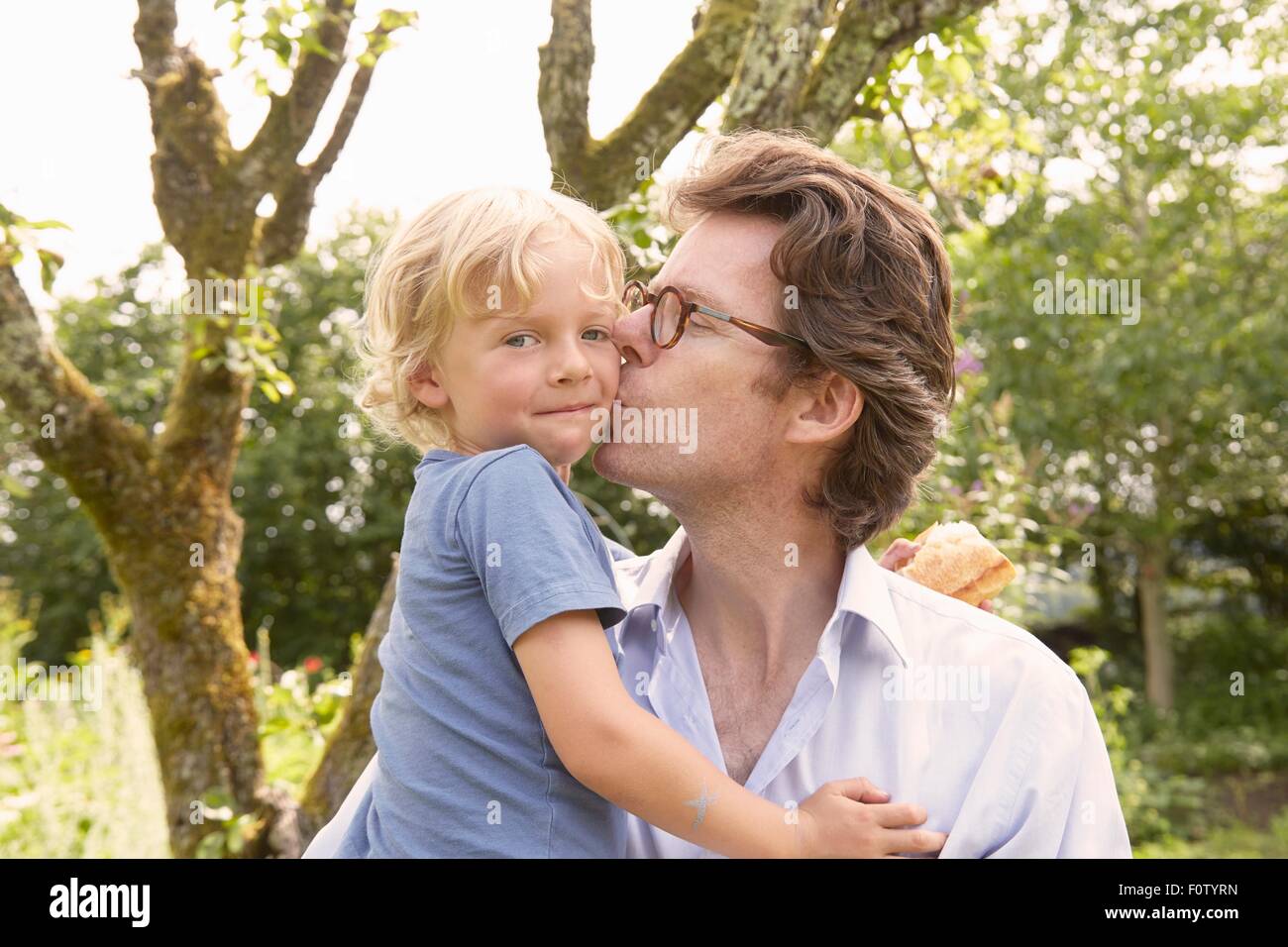 Ritratto di uomo maturo kissing figlio sulla guancia in giardino Foto Stock