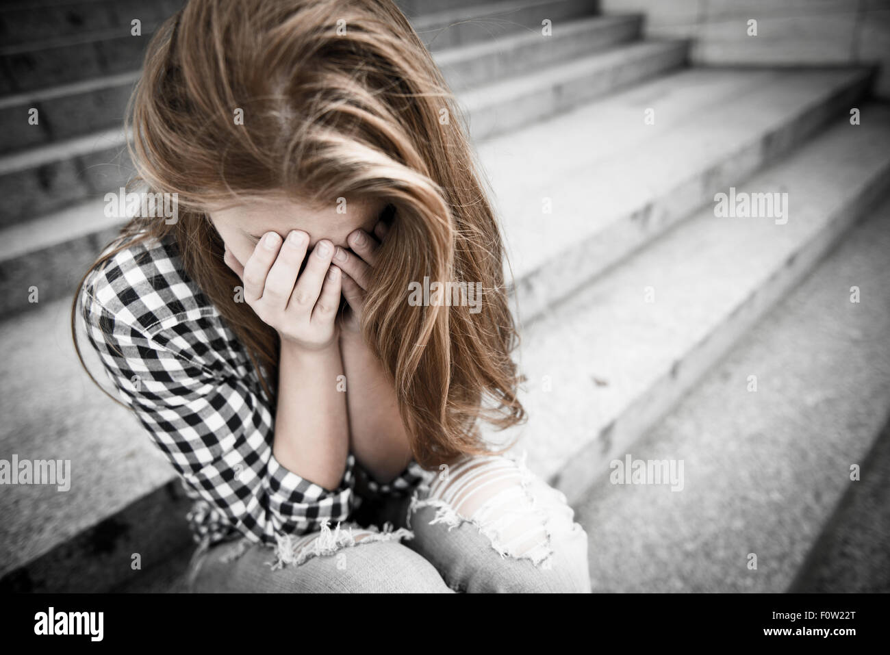 Infelice adolescente depresso con la faccia in mani seduti all'aperto Foto Stock