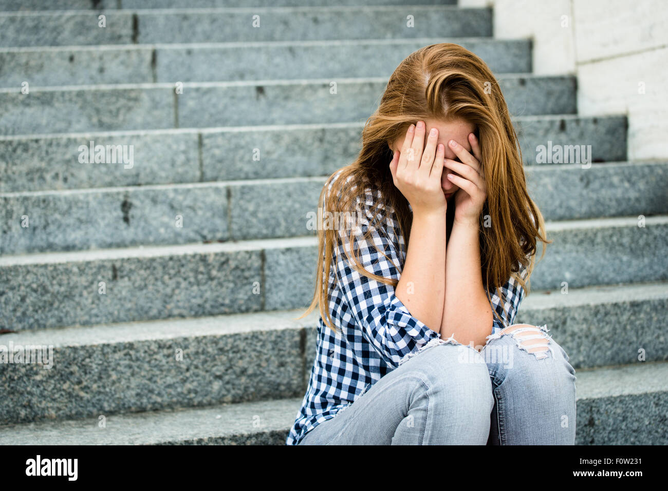 Infelice adolescente depresso con la faccia in mani seduti all'aperto Foto Stock