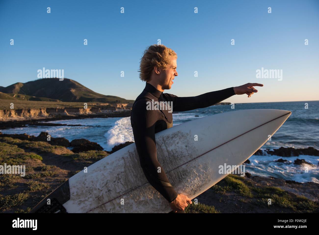 Giovane maschio surfer di segnalare al mare da una scogliera Foto Stock