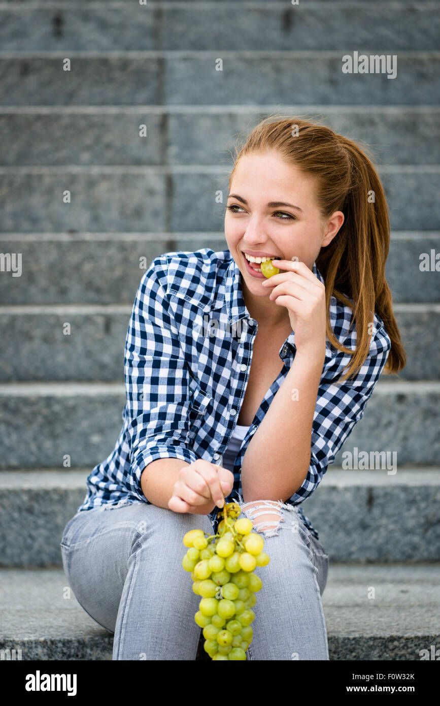 Giovane donna - ragazza adolescente mangiare uva outdoor seduta sulle scale Foto Stock