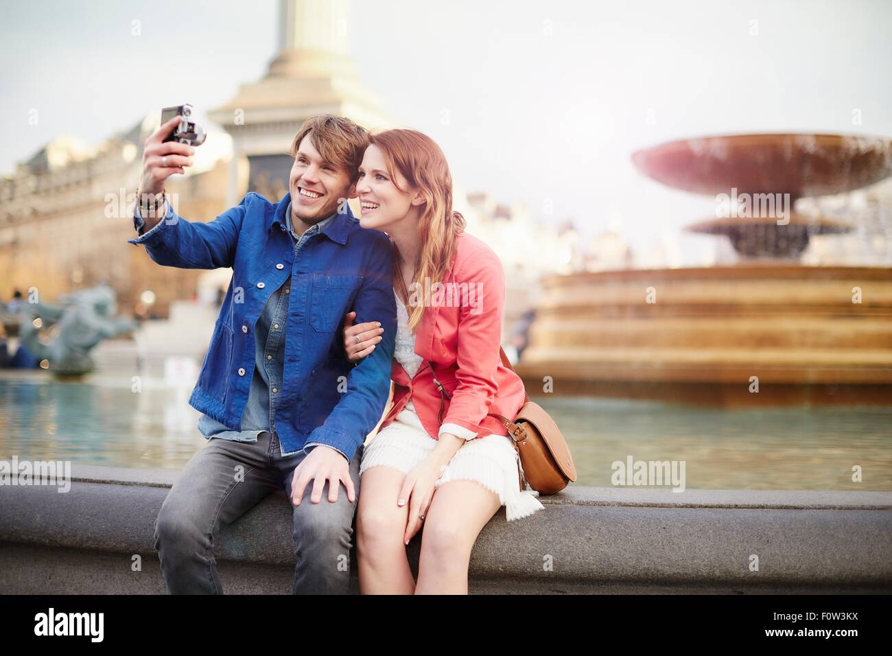 Giovane tenendo la fotocamera selfie a Trafalgar Square fontana, London, Regno Unito Foto Stock