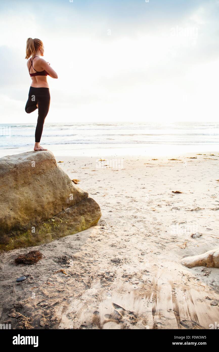Metà donna adulta struttura pratica yoga pone sulla spiaggia rock Foto Stock