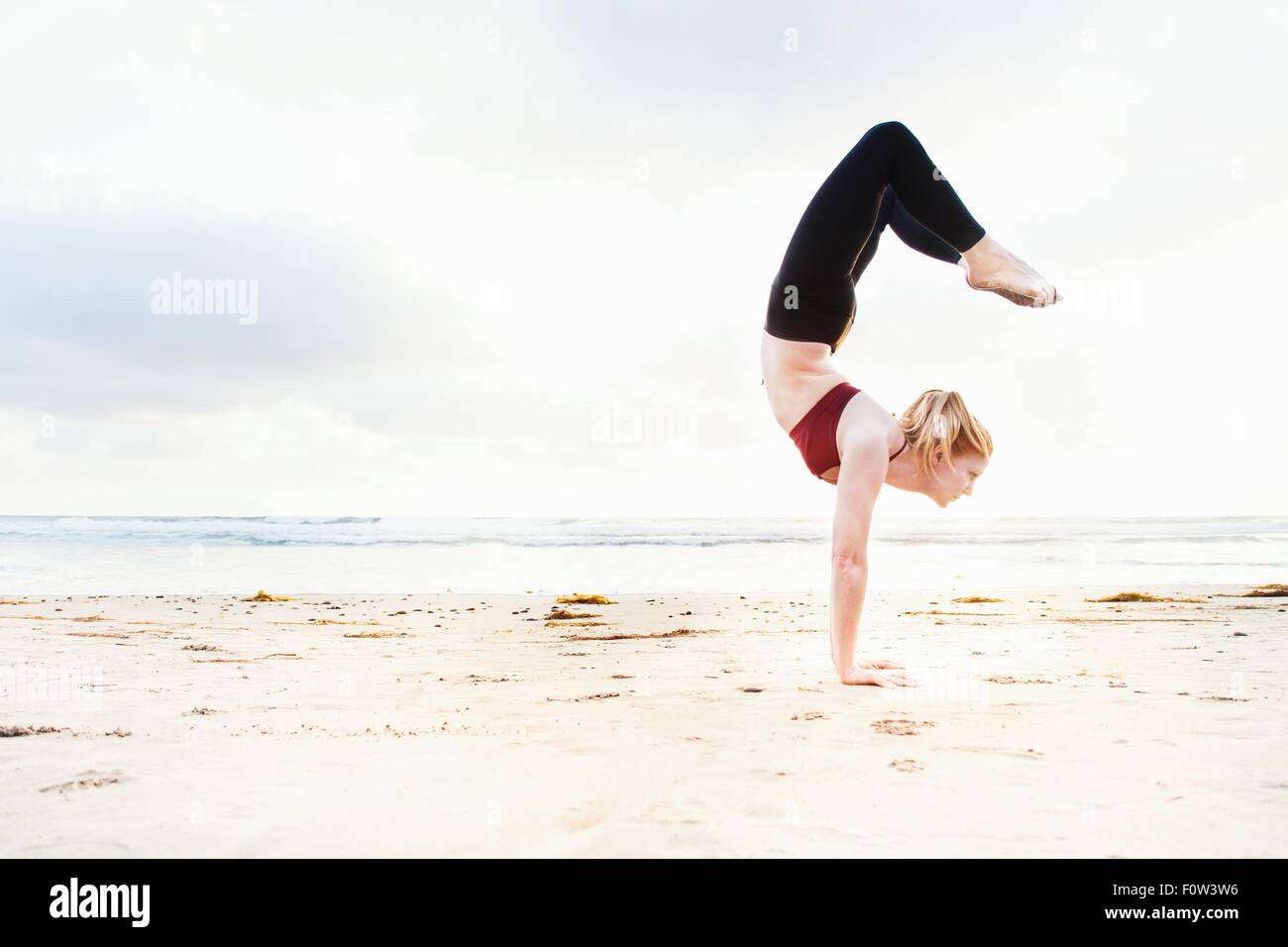 Metà donna adulta praticando yoga handstand posizione sulla spiaggia Foto Stock