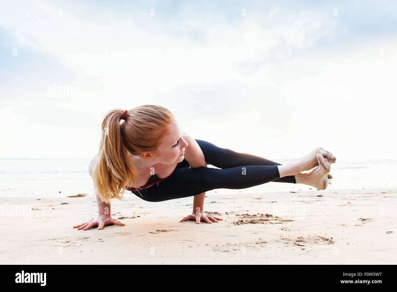 Metà donna adulta in bilico in posizione di yoga sulla spiaggia Foto Stock