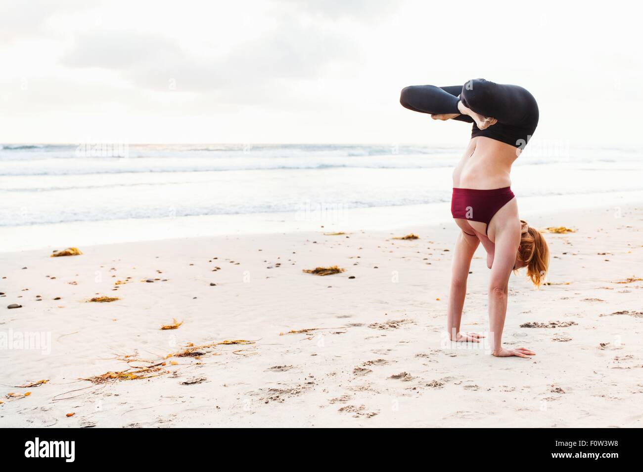 Metà donna adulta capovolto in posizione di yoga sulla spiaggia Foto Stock