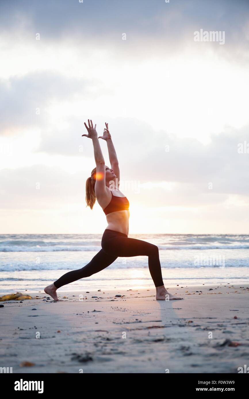 Metà donna adulta guerriero di praticare lo yoga pone sulla spiaggia al tramonto Foto Stock