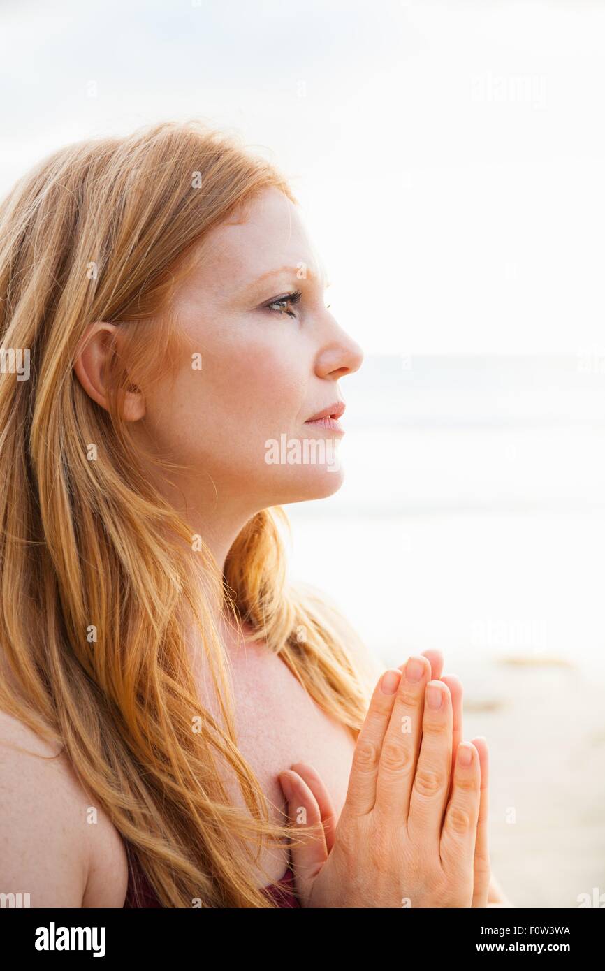 In prossimità di metà donna adulta la pratica dello yoga con le mani insieme sulla spiaggia Foto Stock