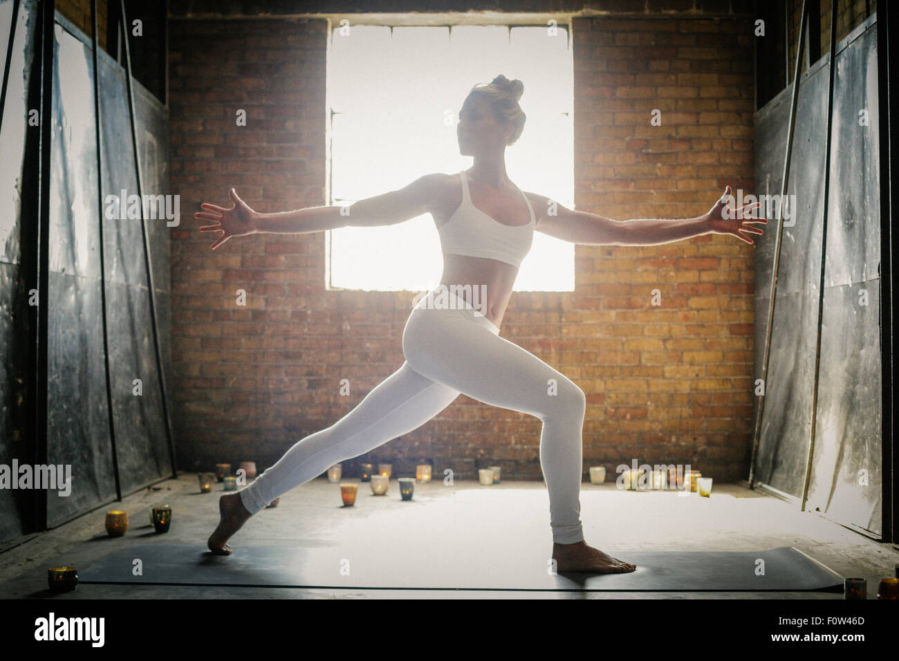 Una donna bionda in piedi su un materassino yoga circondata da candele, fare yoga, le braccia aperte. Foto Stock