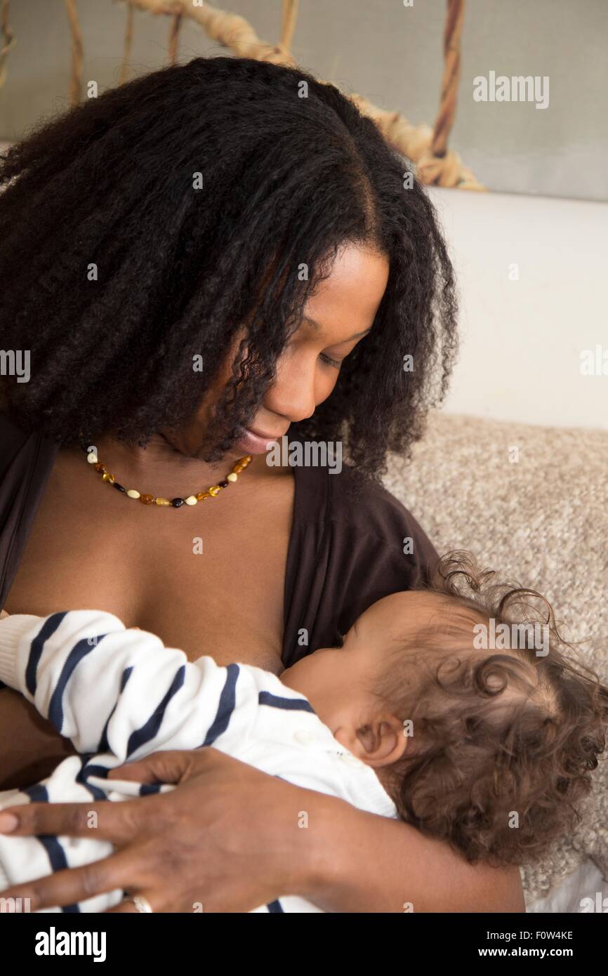 Metà donna adulta allattamento al seno del bambino figlia sul divano Foto Stock