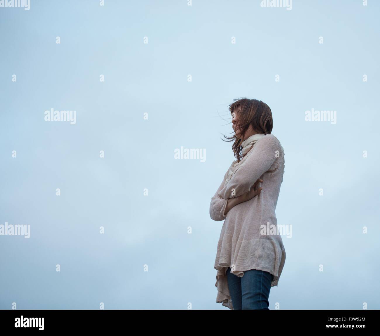 Basso angolo di visione della donna con le braccia incrociate e cielo nuvoloso Foto Stock