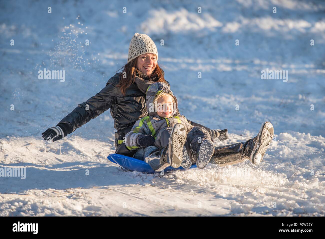 Ritratto di sorridere la madre e il figlio lo slittino in discesa nella neve Foto Stock