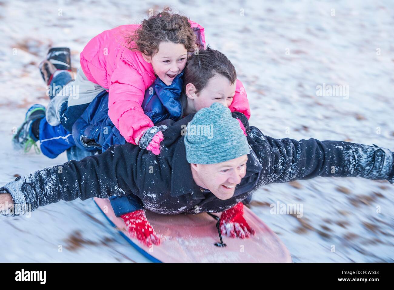 Ritratto di padre e figlio e figlia recante sulla parte superiore di ogni altro cavalcare slittino giù per la collina Foto Stock