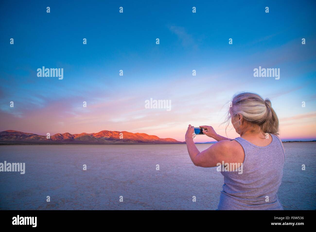 Donna prendendo smartphone fotografia di saline e montagne distanti al tramonto, Calico, CALIFORNIA, STATI UNITI D'AMERICA Foto Stock