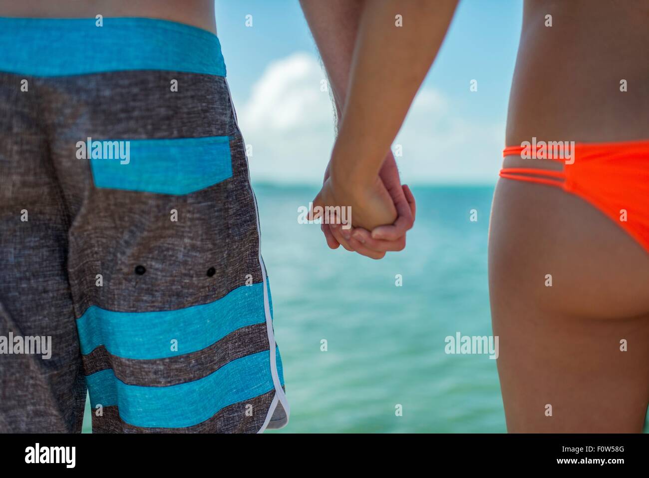 Vista ritagliata della coppia giovane tenendo le mani nella parte anteriore di mare blu, Islamorada, Florida, Stati Uniti d'America Foto Stock