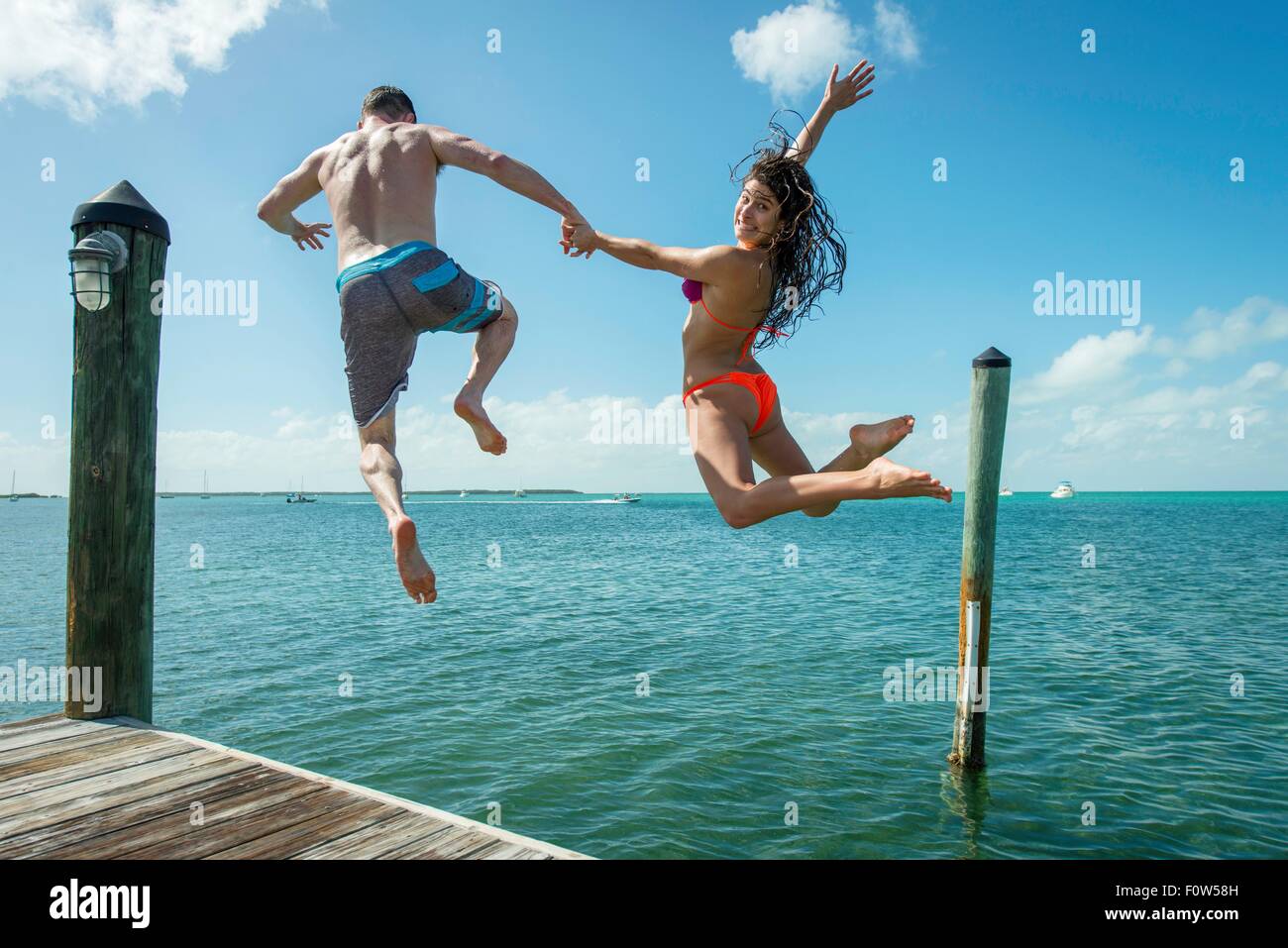 Vista posteriore della coppia giovane salto dal molo sul mare, Islamorada, Florida, Stati Uniti d'America Foto Stock