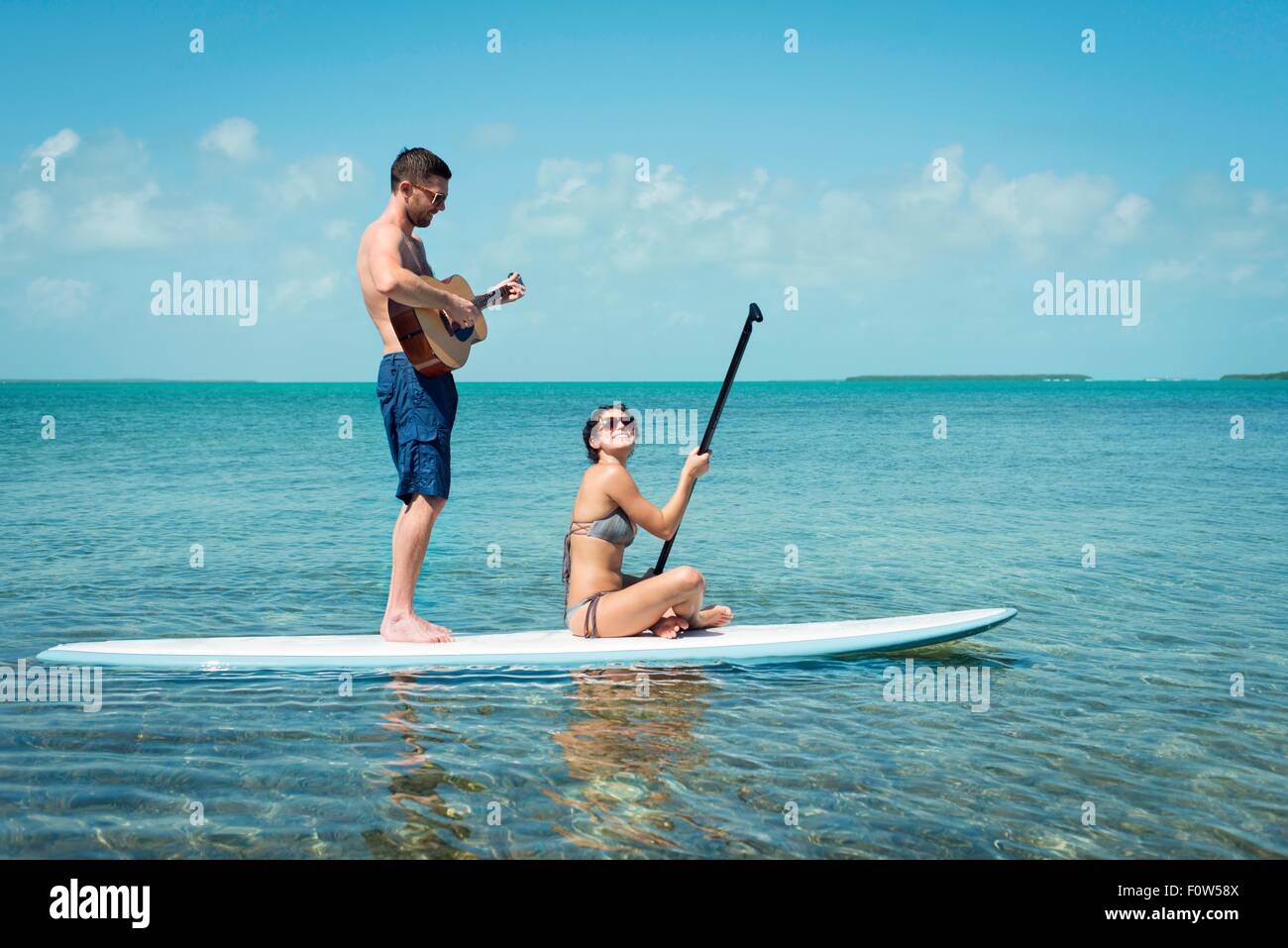Coppia giovane paddleboarding e suonare la chitarra, Islamorada, Florida, Stati Uniti d'America Foto Stock