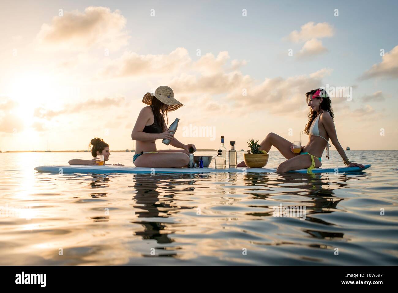 Due giovani donne la preparazione di cocktail su paddleboard al tramonto, Islamorada, Florida, Stati Uniti d'America Foto Stock