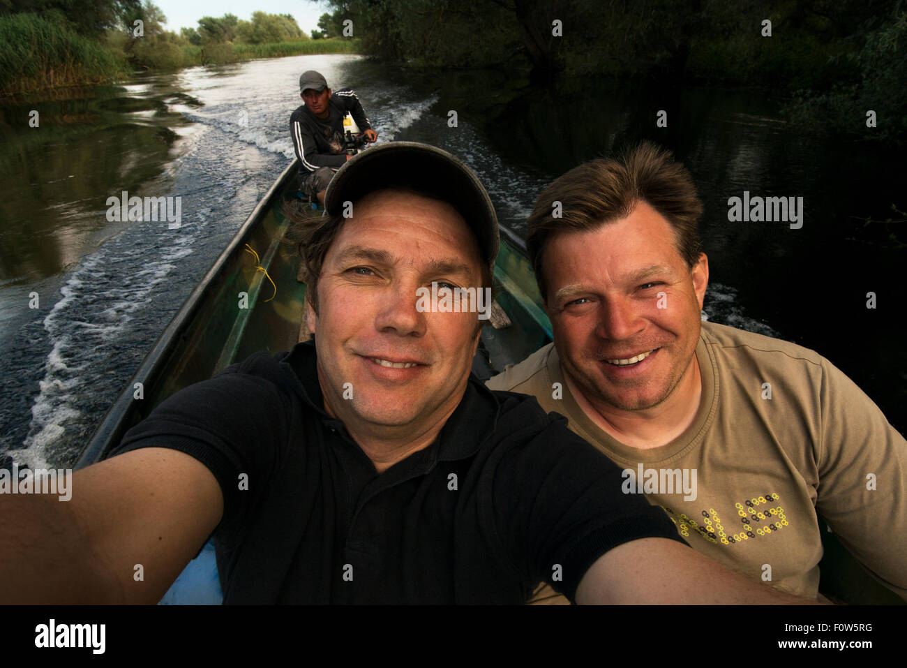 Fotografo Magnus Lundgren tenendo selfie con Christian Mititelu e fisherman Florin Moisa in background in barca nel Delta del Danubio, Romania. Giugno 2013. Foto Stock