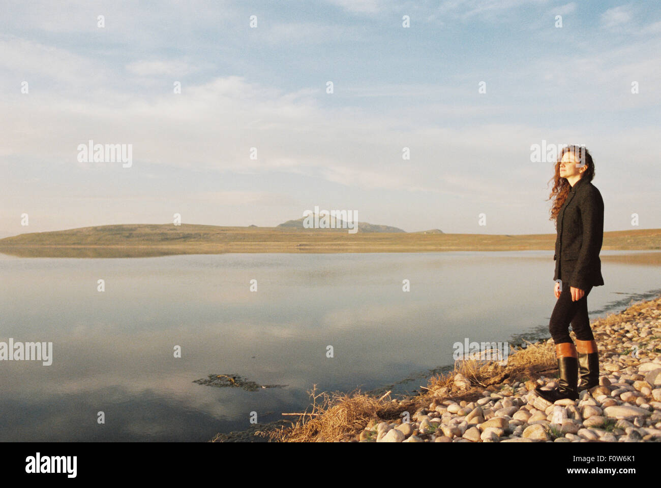 Una donna con capelli ricci in piedi sulla riva di un lago. Foto Stock