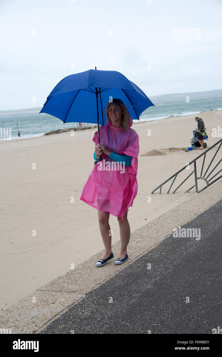 Femmina di vacanzieri con un ombrello e poncho in riva al mare su un umido e ventoso giorno. Bournemouth Inghilterra meridionale REGNO UNITO Foto Stock