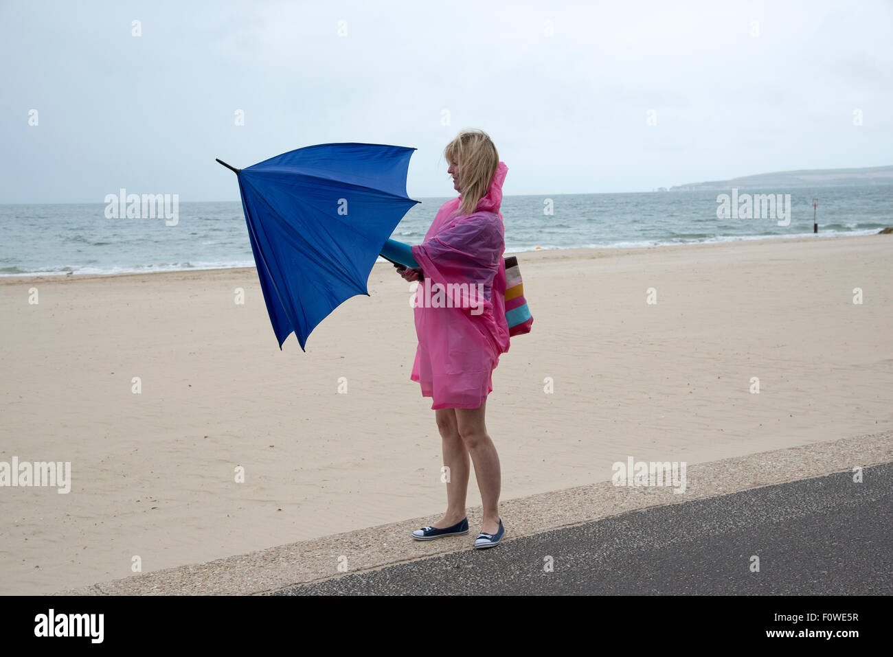 Femmina di vacanzieri con un ombrello e poncho in riva al mare su un umido e ventoso giorno. Bournemouth Inghilterra meridionale REGNO UNITO Foto Stock