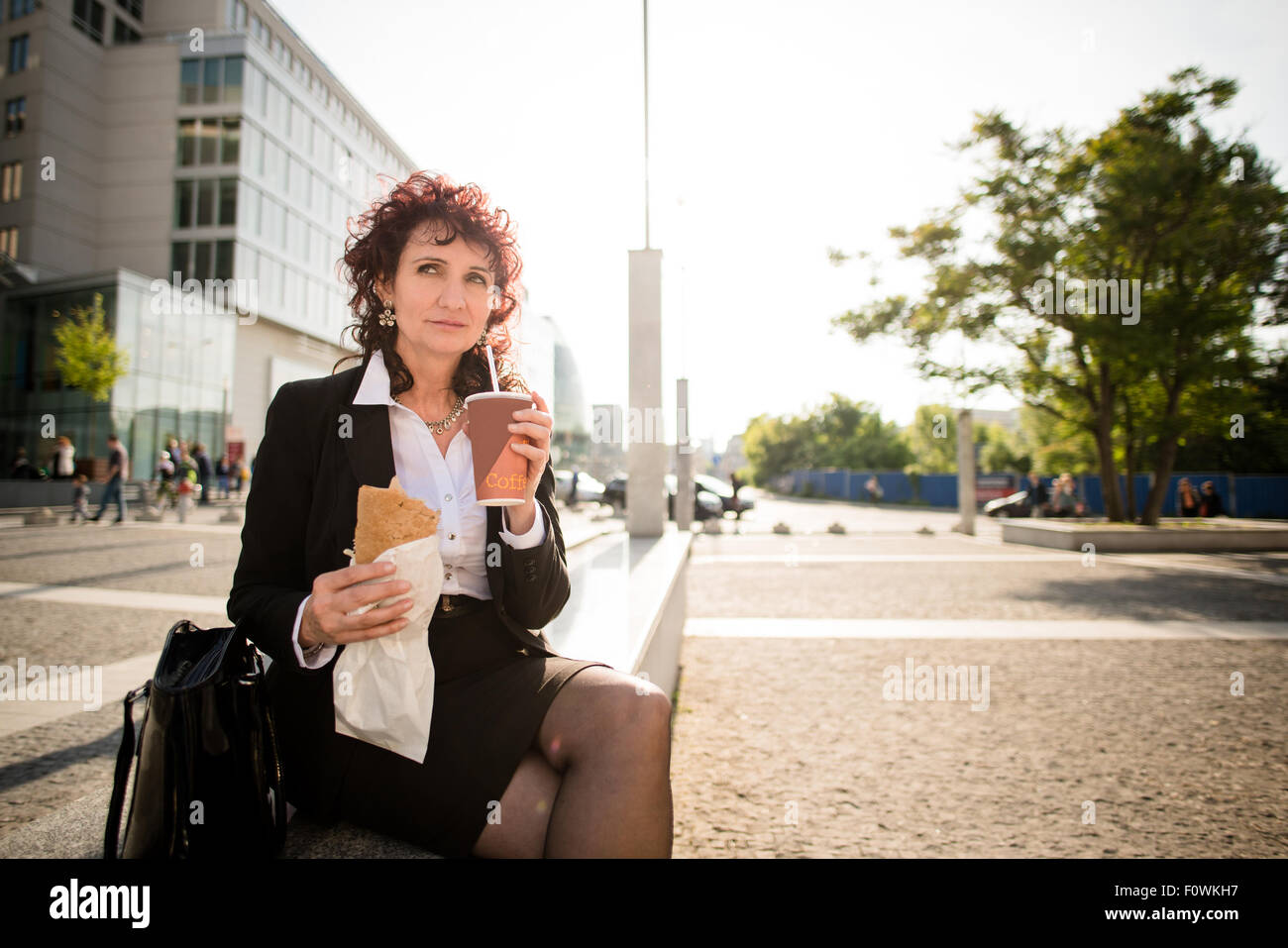 Senior business donna su fast food il pranzo - Bere take-away caffè e mangiare panino in street Foto Stock