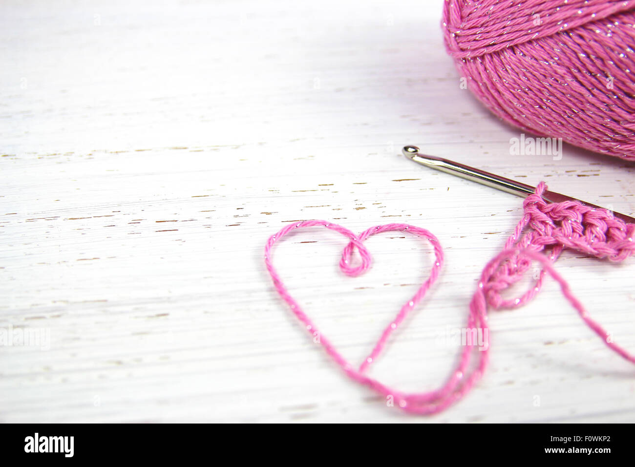 Crochet rosa sfondo con cuore di filato su bianco in legno rustico sfondo con spazio di copia Foto Stock