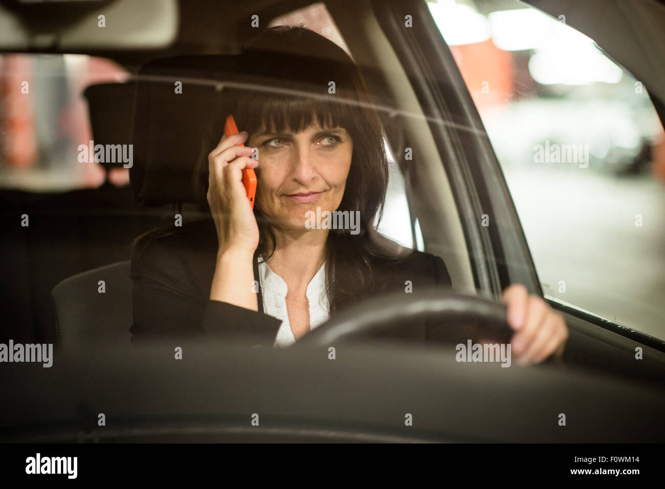 Dettaglio del senior business donna che chiama il telefono cellulare mentre si guida auto a notte - vista attraverso il vetro anteriore Foto Stock