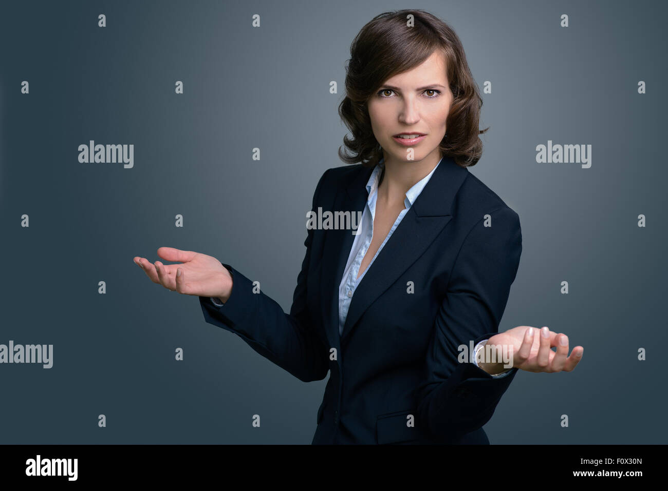 Mezzo Corpo colpo di un confuso giovane imprenditrice con le mani in aria, esaminando la distanza contro il muro grigio. Foto Stock