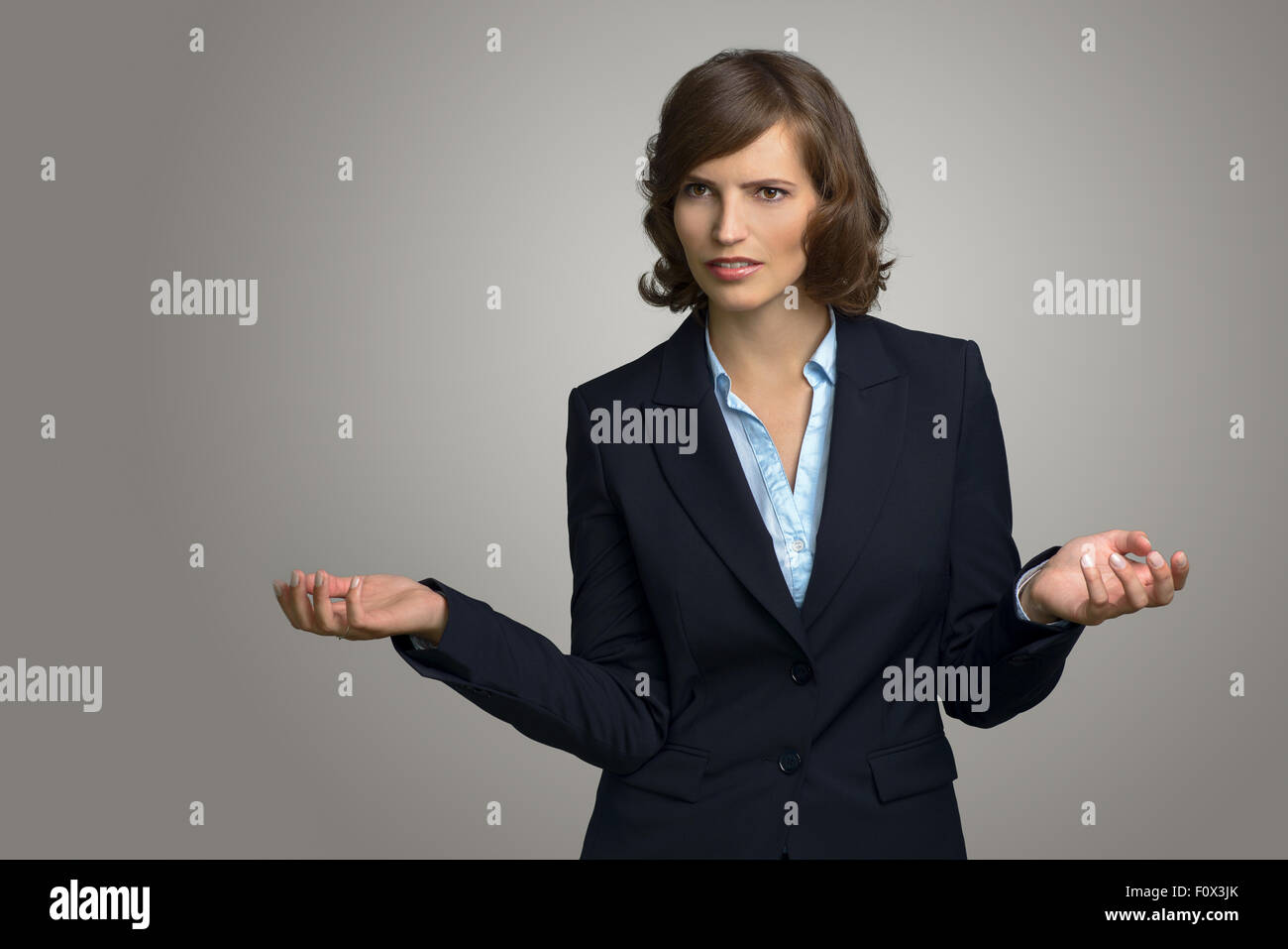 Mezzo Corpo colpo di un confuso giovane imprenditrice con le mani in aria, esaminando la distanza contro il muro grigio. Foto Stock