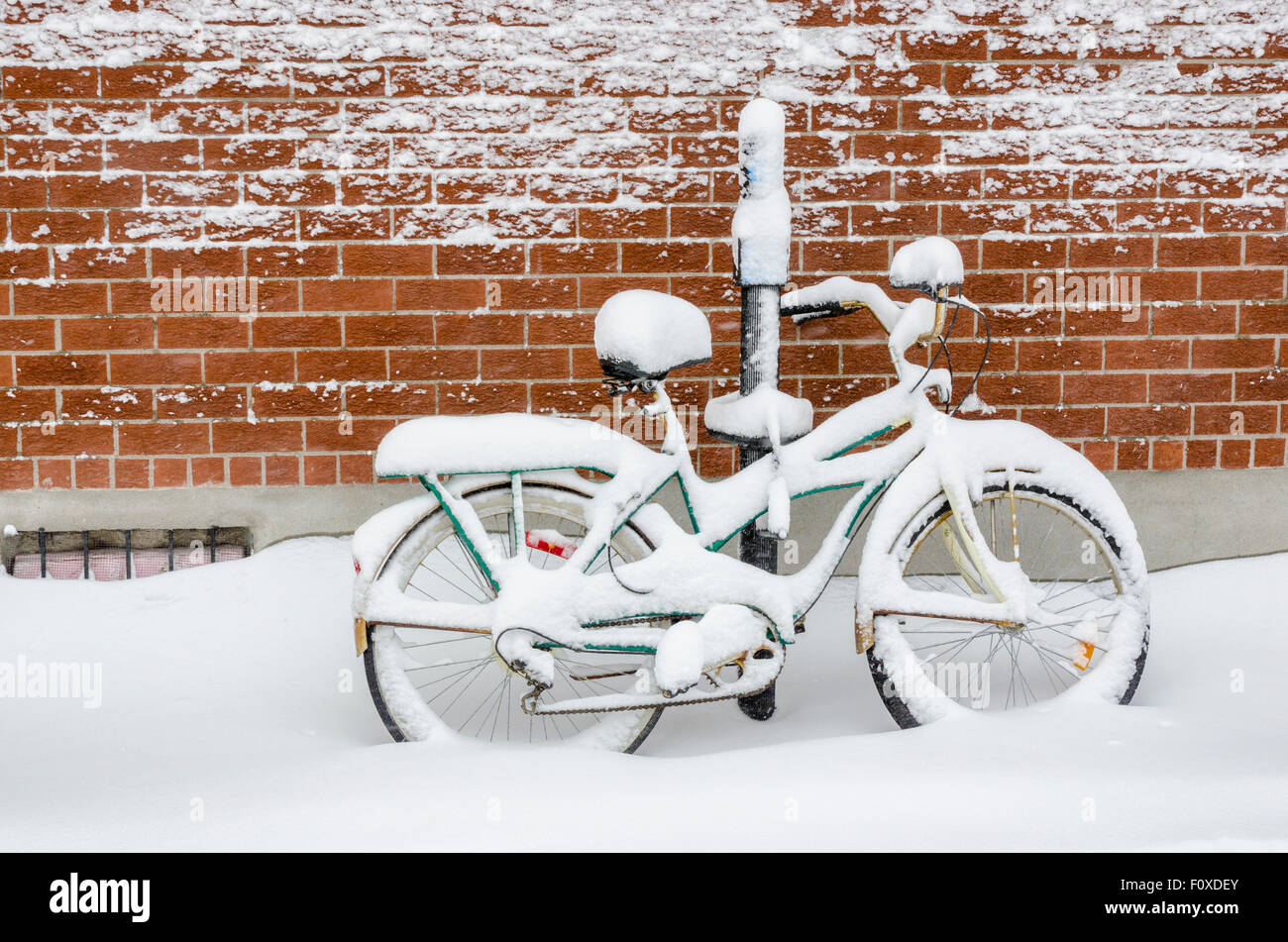 Una bicicletta appoggiata contro un muro di mattoni e coperte di neve fresca dopo una tempesta di neve a Montreal, Canada Foto Stock
