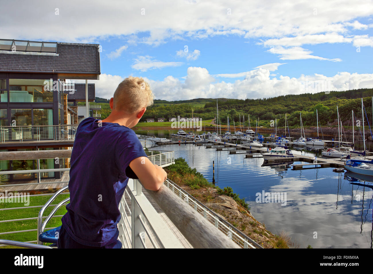 Ragazzo appoggiato su di un balcone che si affaccia sulla Marina Portavadie su la costa ovest della Scozia Foto Stock