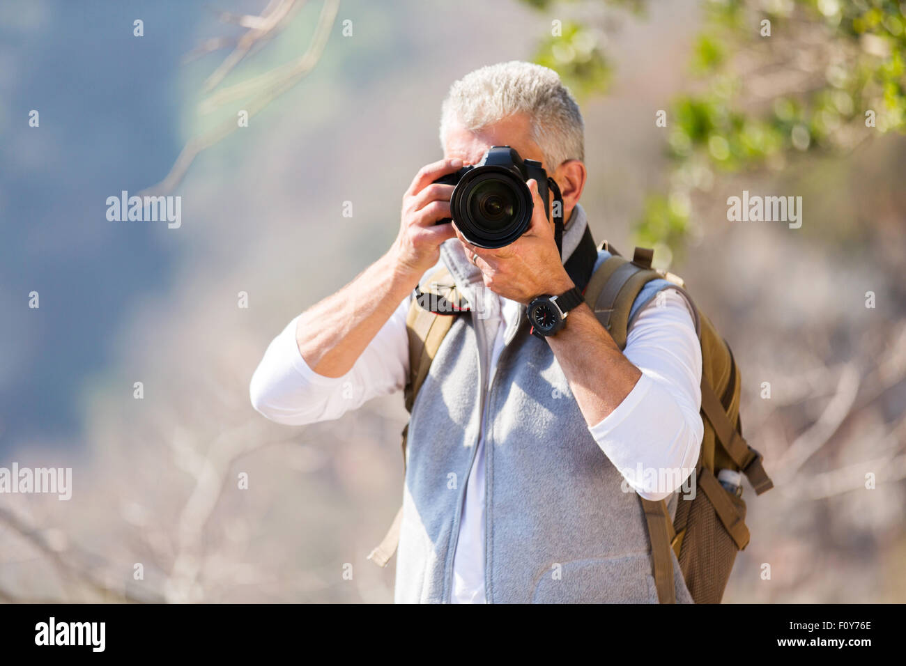 Uomo di mezza età Scattare foto nella valle di montagna con fotocamera reflex digitale Foto Stock