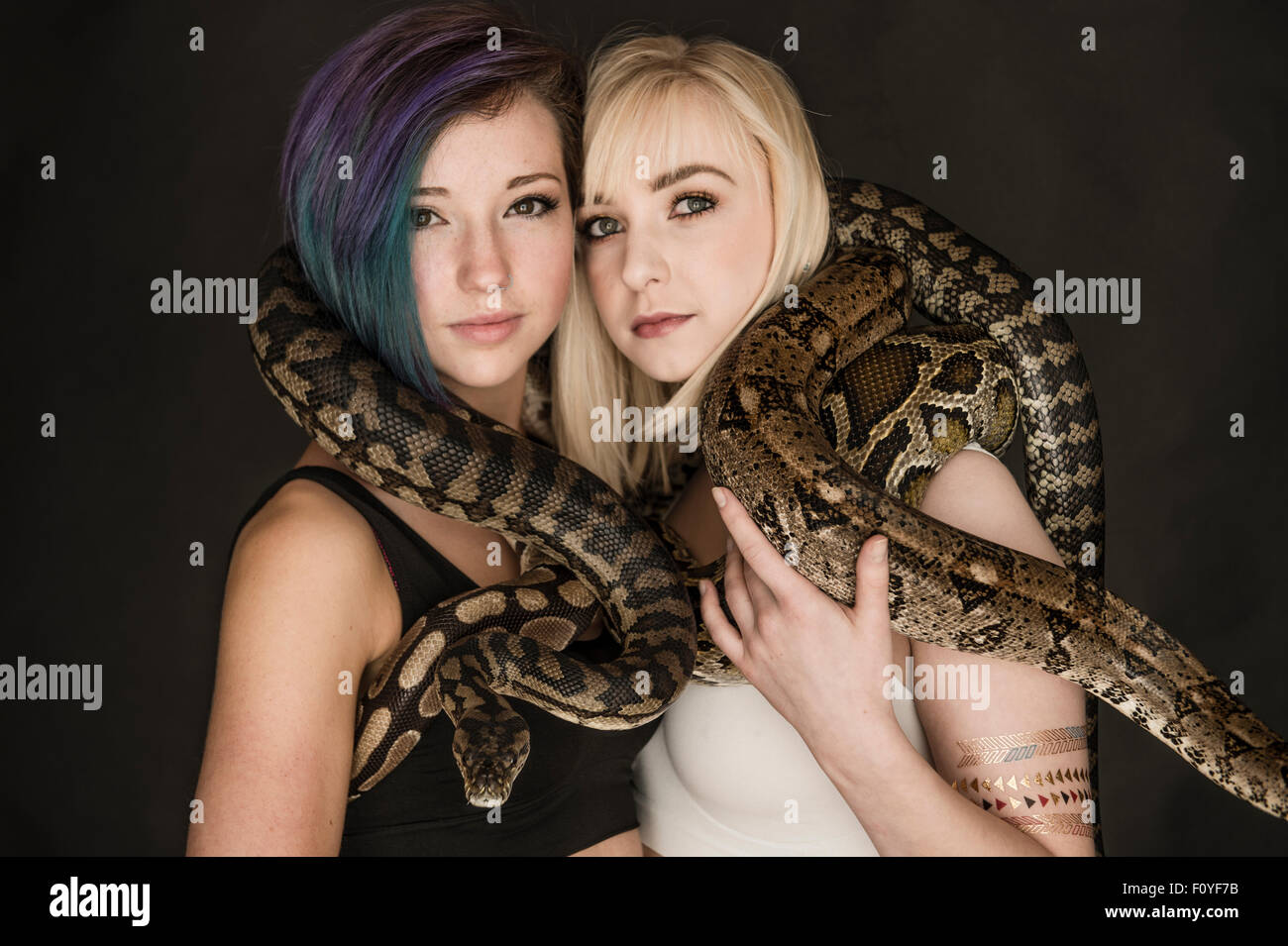 Due giovani donne ragazze femmine in posa con serpenti intrecciano intorno ai loro corpi, UK (non soffre di ophiophobia - La paura dei serpenti) Foto Stock