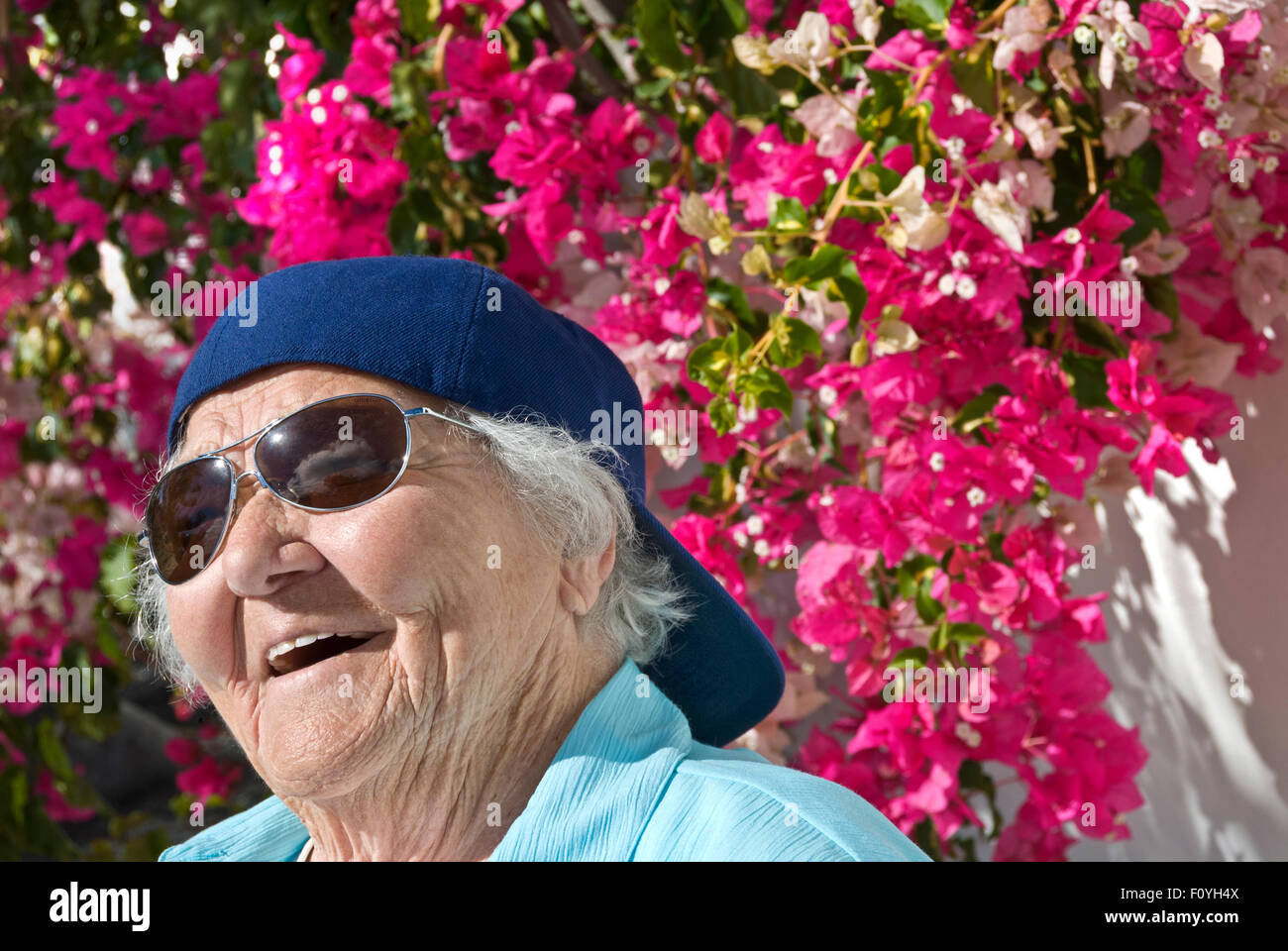 Anziani giardino prendisole felice senior anziana signora "giovani nel cuore' alla moda che indossa il cappello e occhiali da sole nel suo sunny floral villa per vacanze home Foto Stock