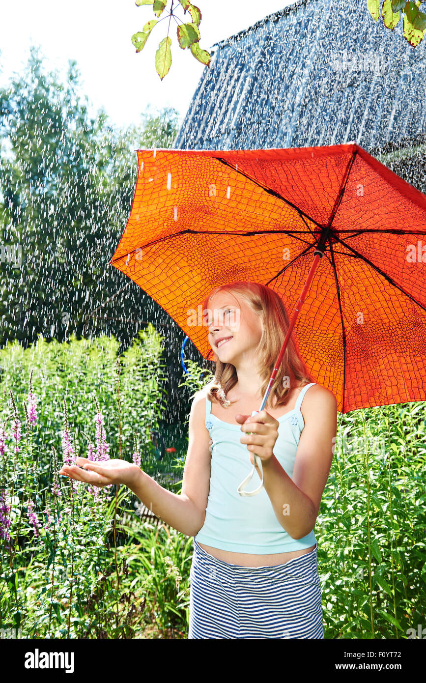 Felice ragazza con ombrello rosso sotto la pioggia di estate Foto Stock