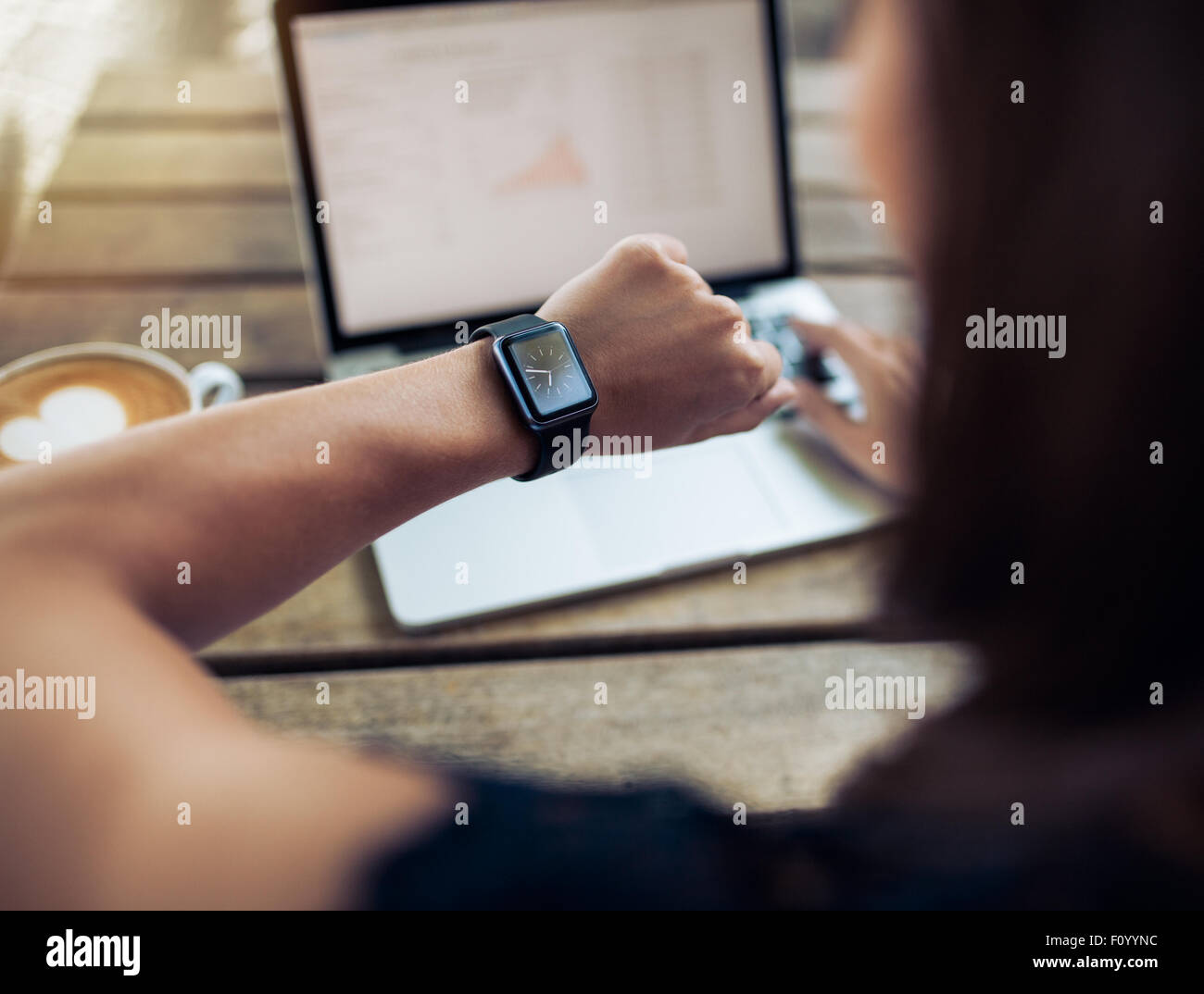 Immagine ravvicinata di una donna di controllo ora sul suo smartwatch. Donna seduta al cafe con un portatile e una tazza di caffè. Foto Stock